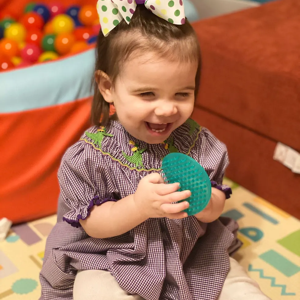 Toddler girl wearing purple bubble smiles while holding a green spiky sensory disc.