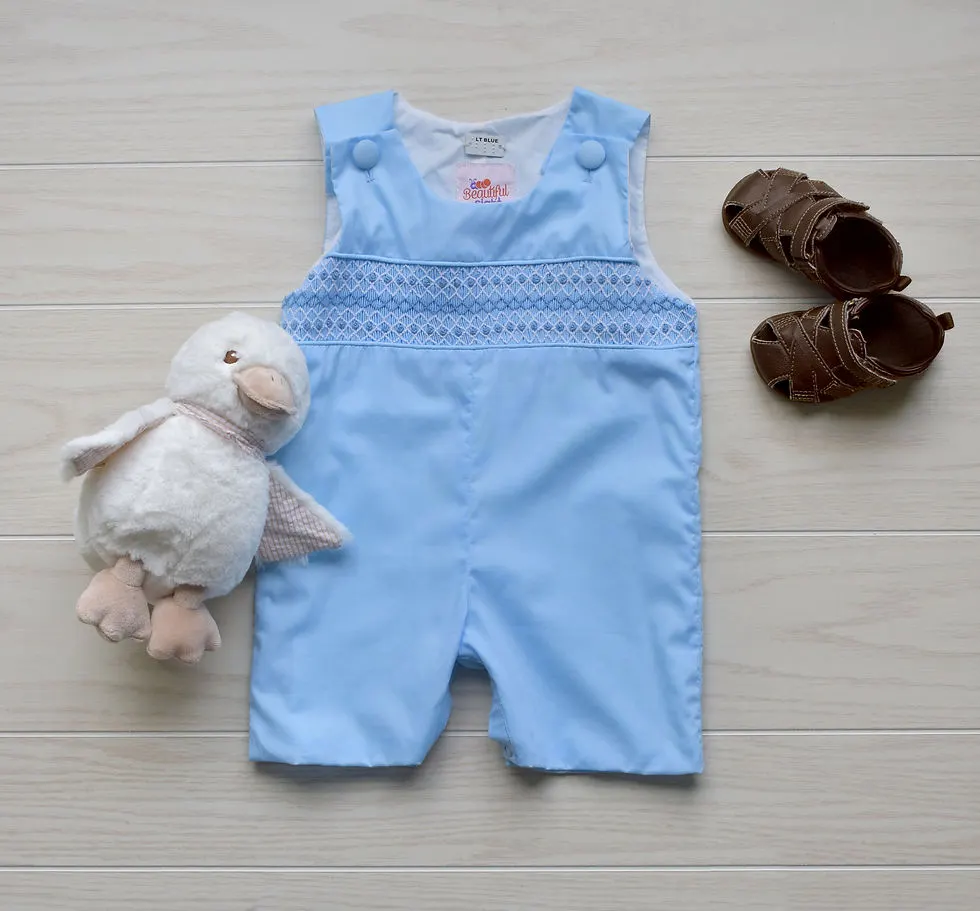 Baby blue shortall with blue & white smocking across the chest. A white stuffed duck & brown shoes lay on either side.