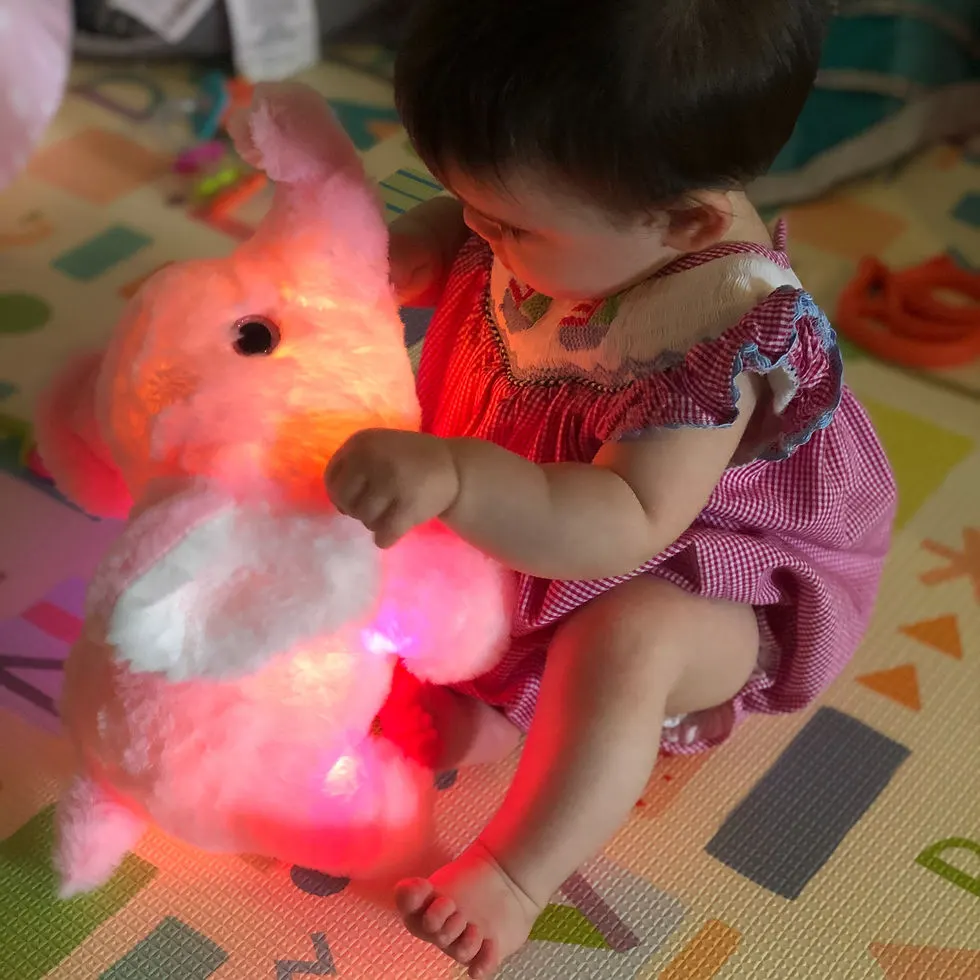 Infant girl hold stuffed pink elephant that is lit up