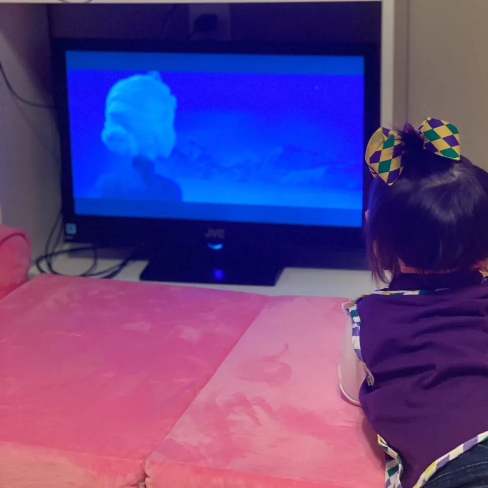 Toddler girl laying on pink couch chair watching Frozen on TV